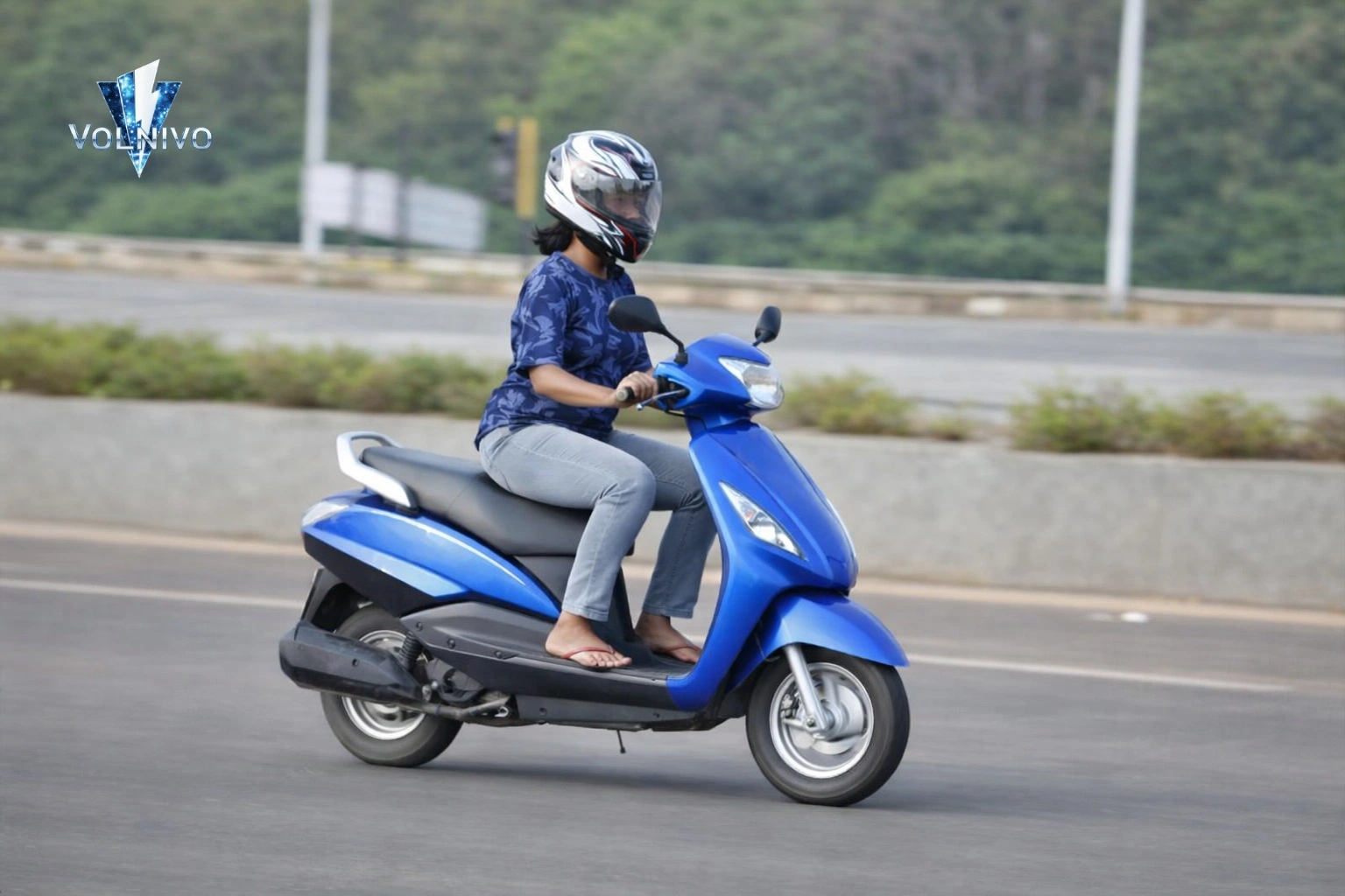 Female scooter rider wearing helmet riding blue scooter on Pakistan city road in 2026