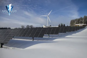 Solar panels farm in snowy landscape near wind turbine: how long do solar batteries last?